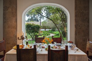 A dining table set with plates, glasses, and a candelabra, overlooking a garden with a pathway and trees.