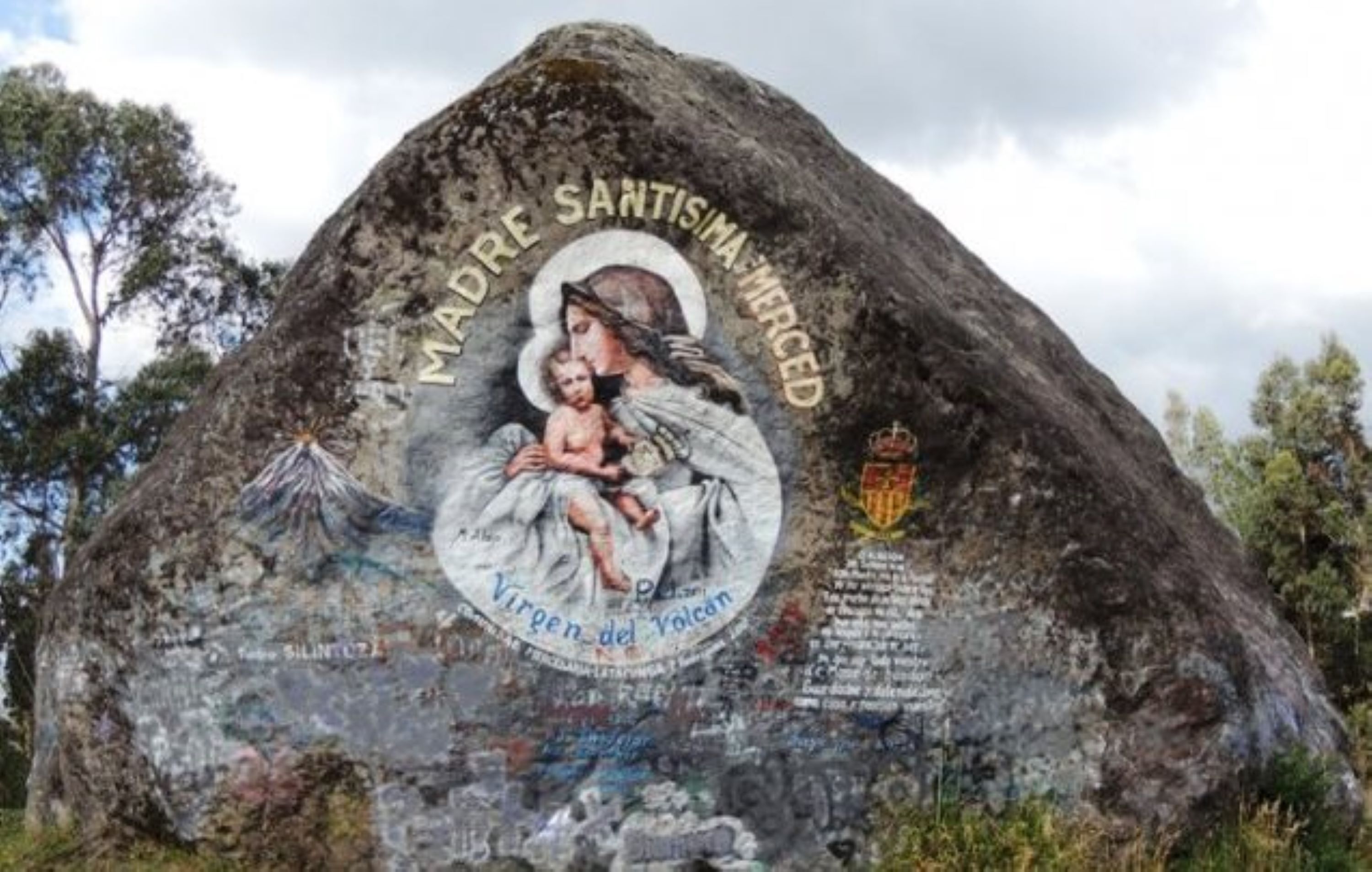 A large rock with a mural of a woman holding a child, surrounded by trees.