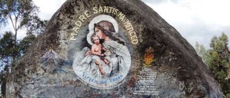 A large rock with a mural of a woman holding a child, surrounded by trees.