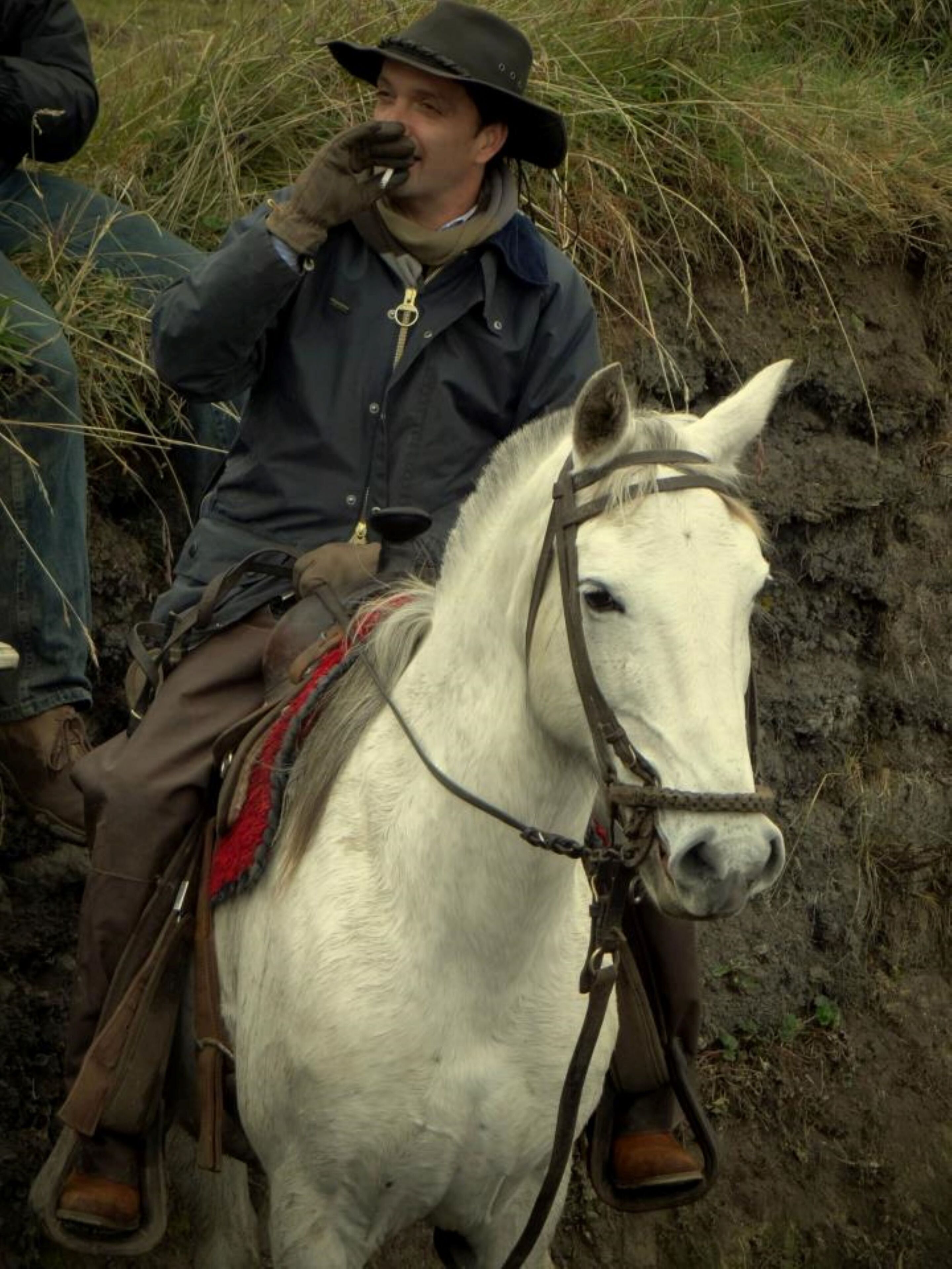 A person riding a white horse with a saddle and bridle.