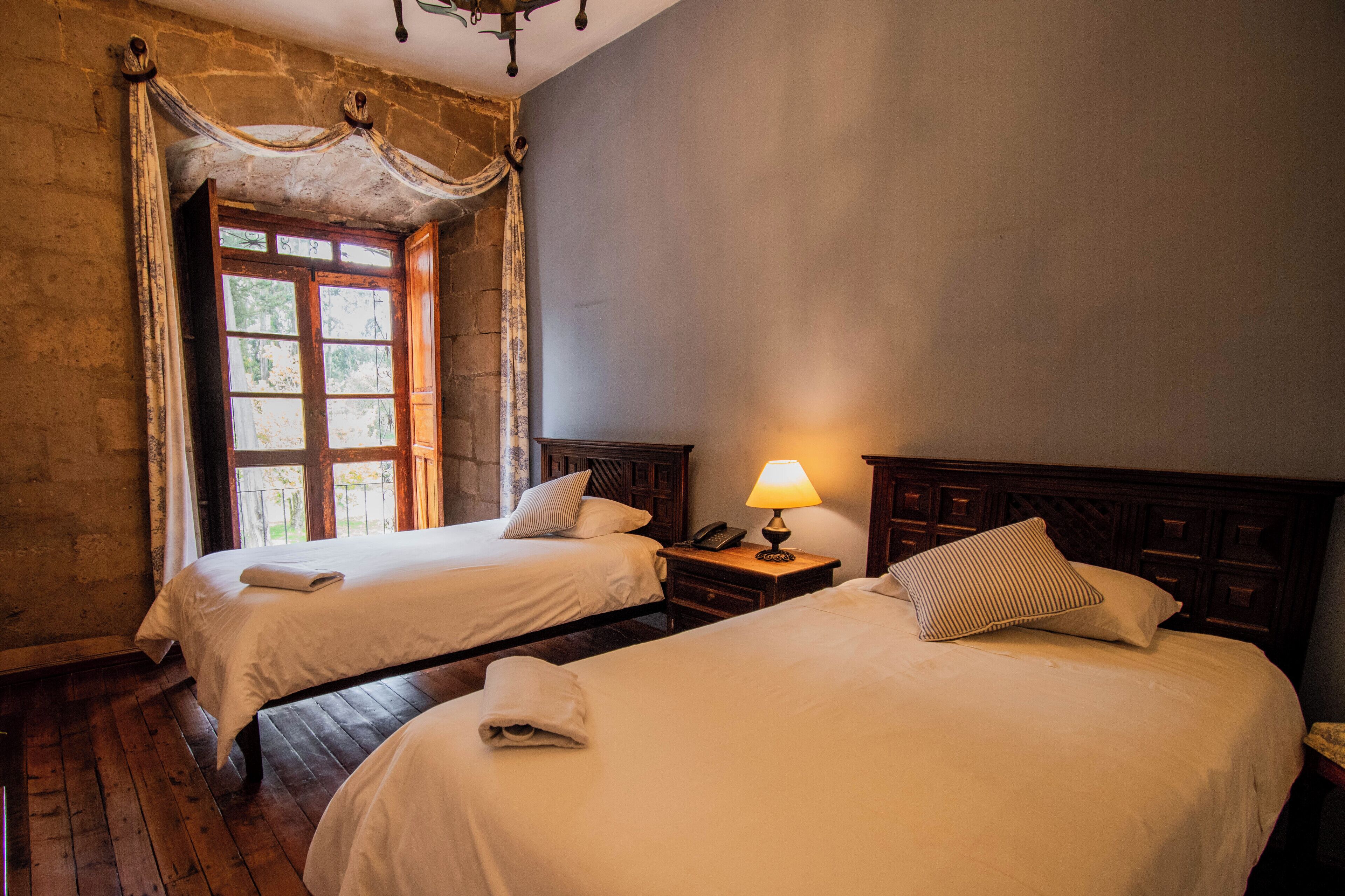 Une chambre avec deux lits, un plancher en bois, un mur en pierre et une fenêtre avec des rideaux.