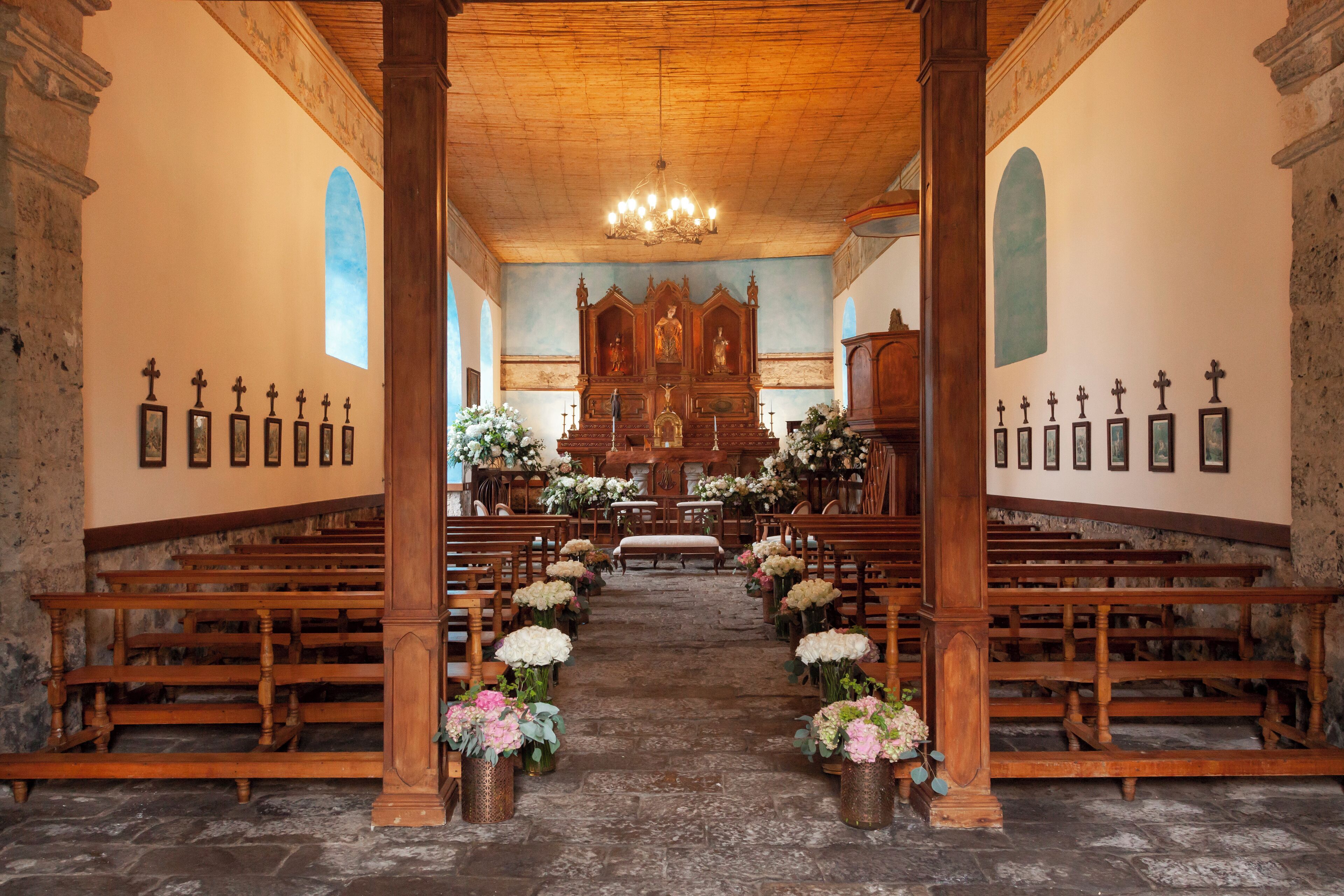 An interior of a church with wooden pews, a central aisle, and floral arrangements.