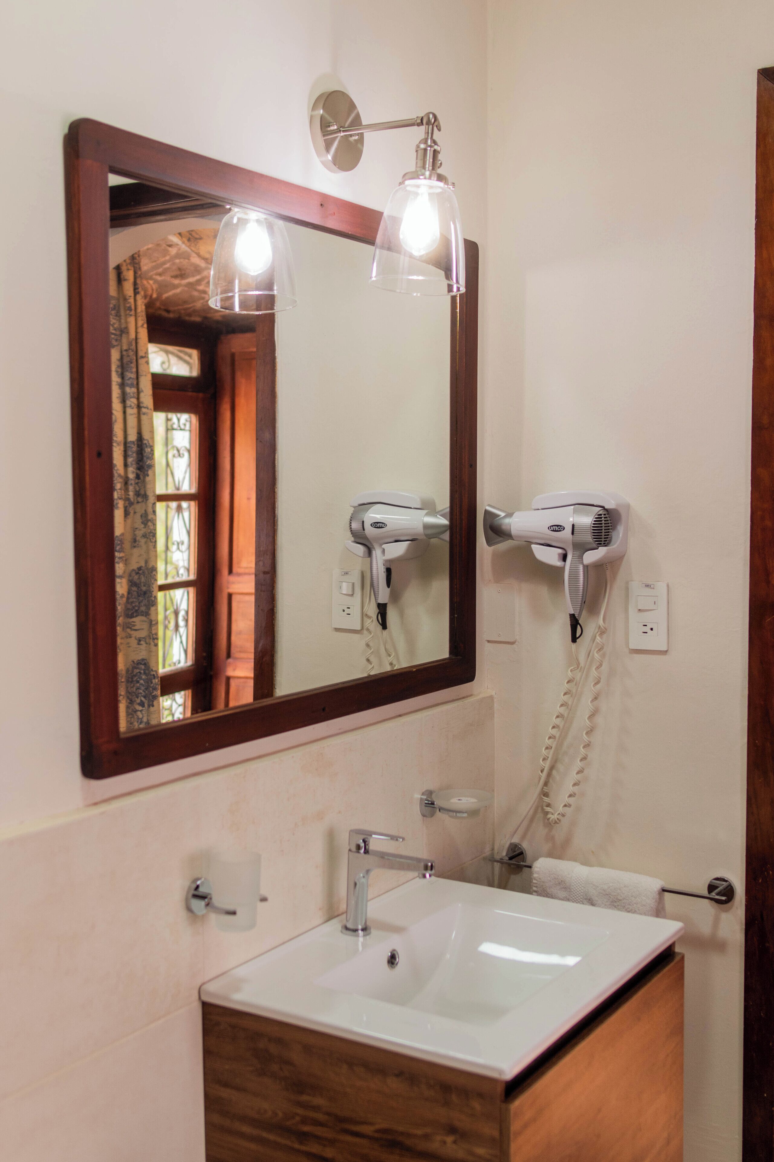 A bathroom with a large mirror, two hair dryers, a sink, and a towel rack.