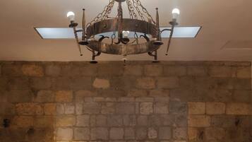 A bedroom with a stone wall, a bed with floral bedding, two bedside lamps, and a chandelier.