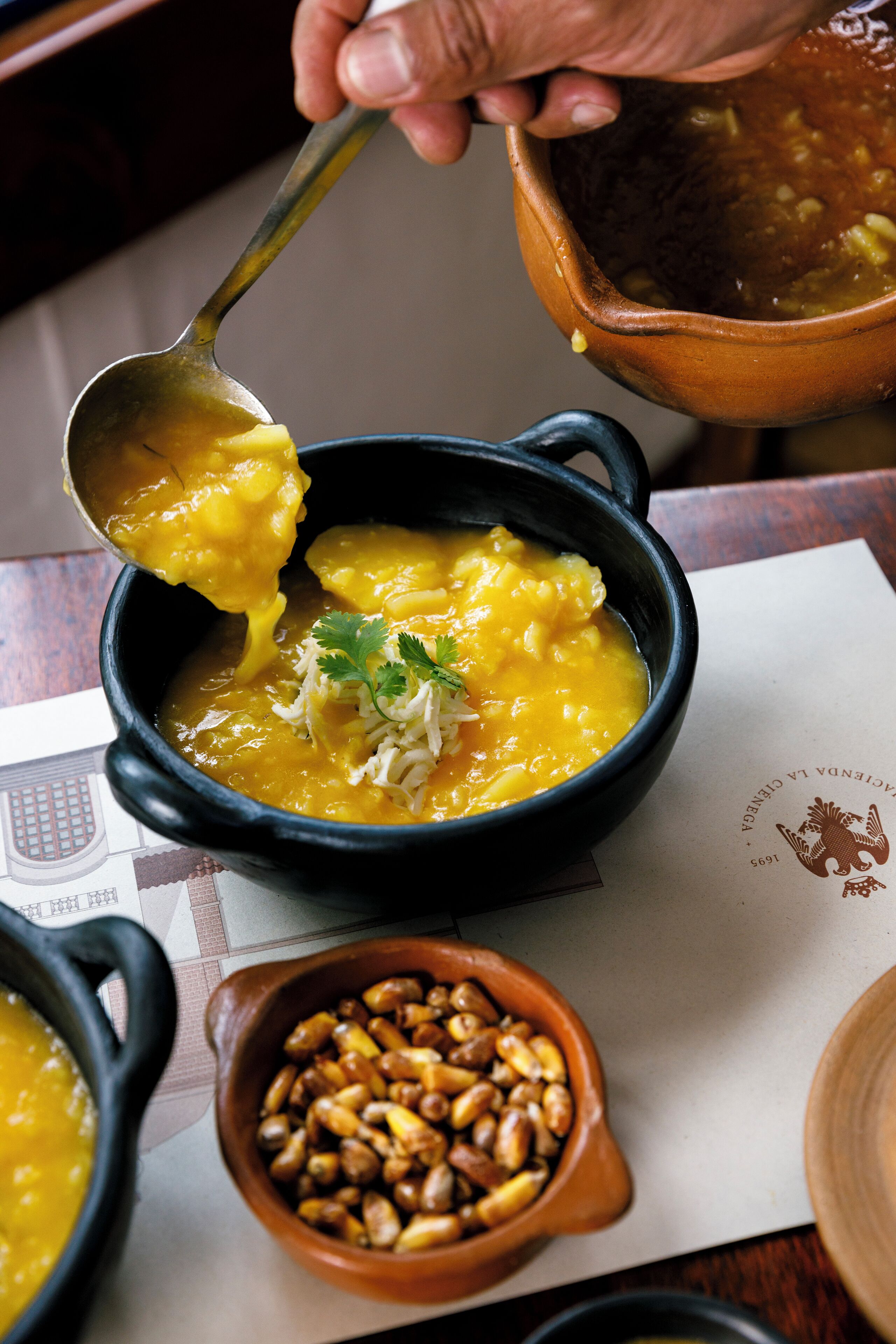 Eine Schüssel Suppe, ein Löffel hebt einen Teil davon, auf einem Tisch zusammen mit einer Speisekarte und einer kleinen Schüssel Nüsse.