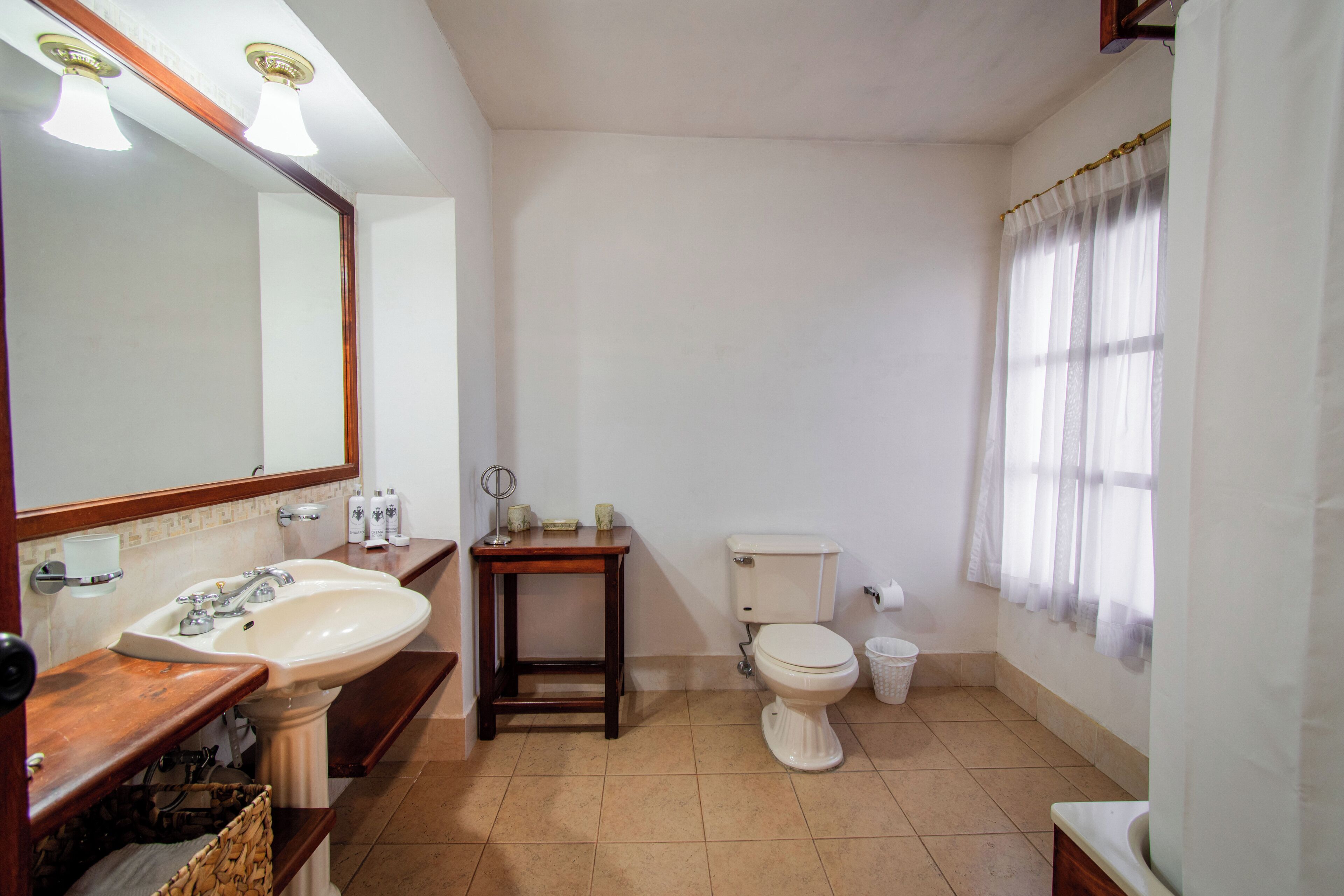 Un baño con lavamanos, espejo, inodoro y una pequeña mesa.