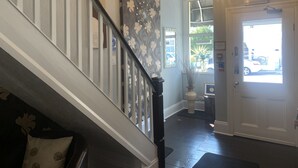 A staircase with a handrail, a chandelier, a door with a fire exit sign, and a window with a view of the outside.