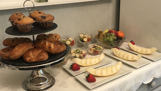 A buffet table with pastries, fruits, and a fruit bowl.