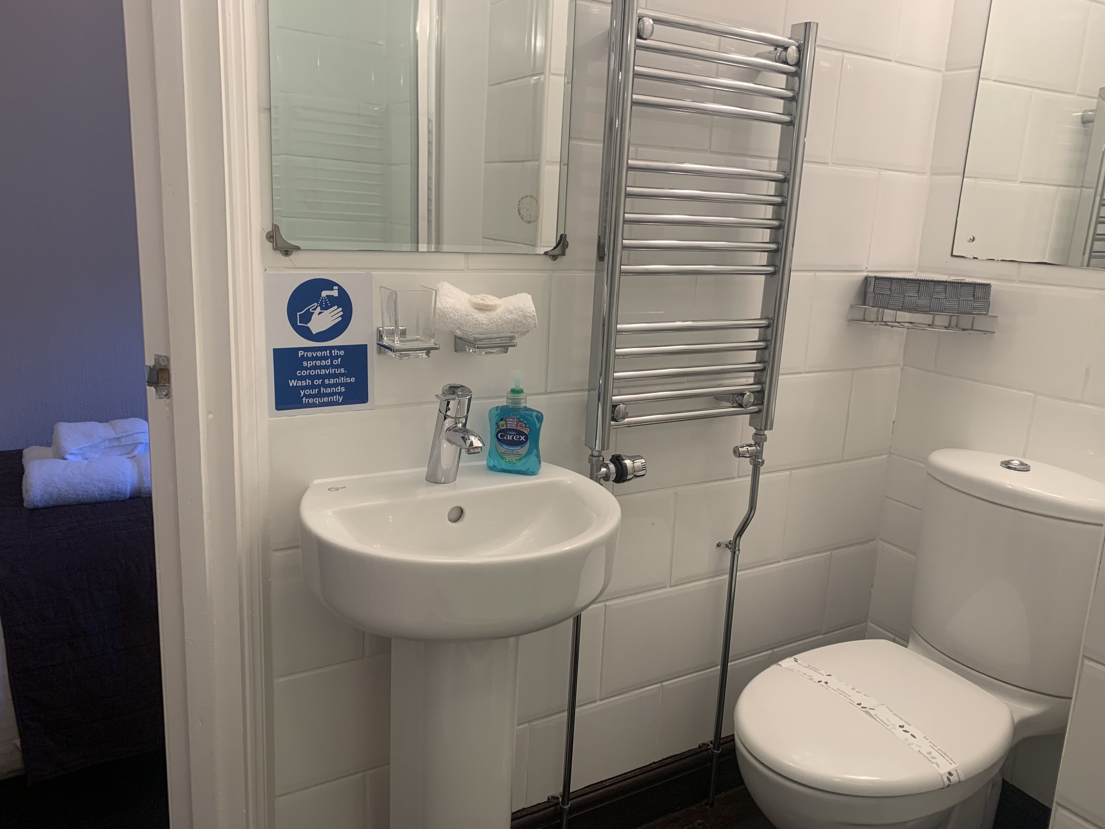 Un baño con un lavabo blanco, un espejo, un perchero para toallas y un inodoro.