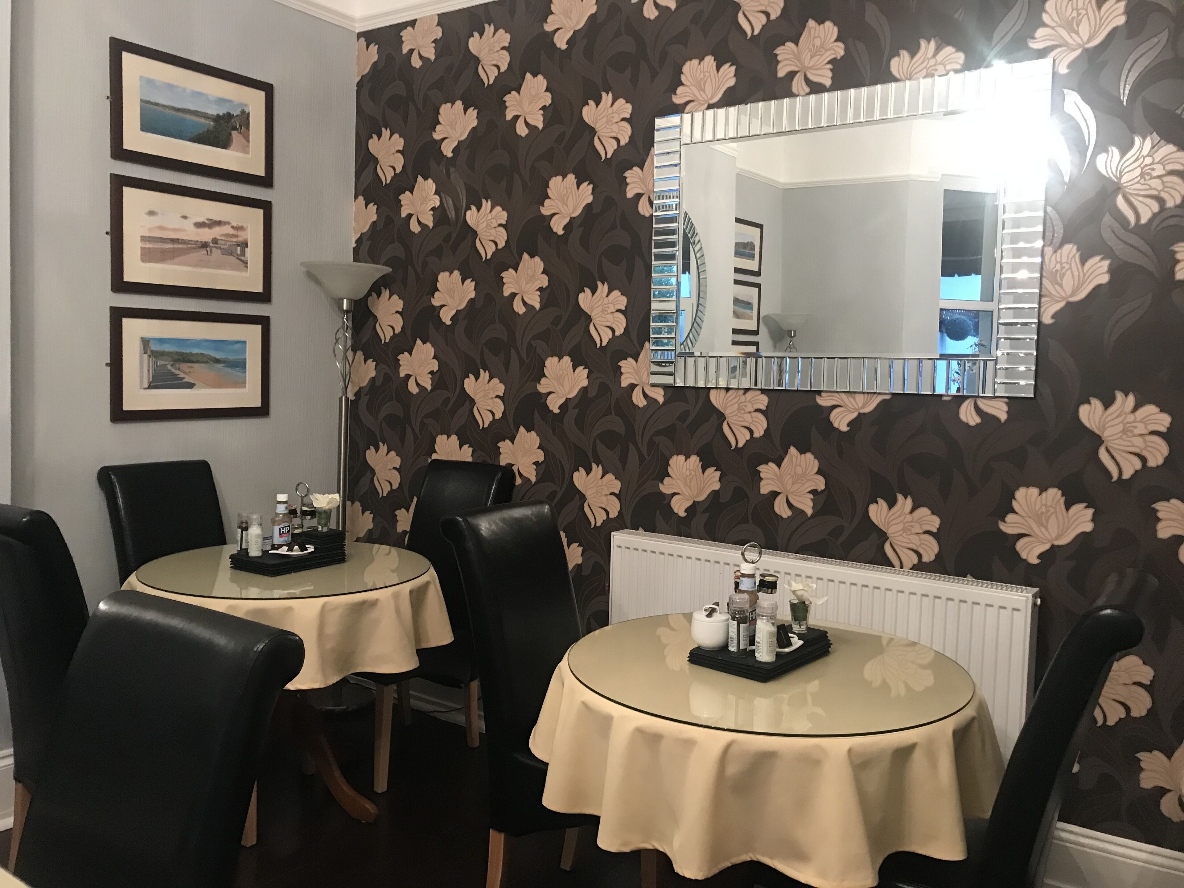 Un espace repas comprenant deux tables rondes, des chaises noires, des tableaux encadrés accrochés au mur et un grand miroir.