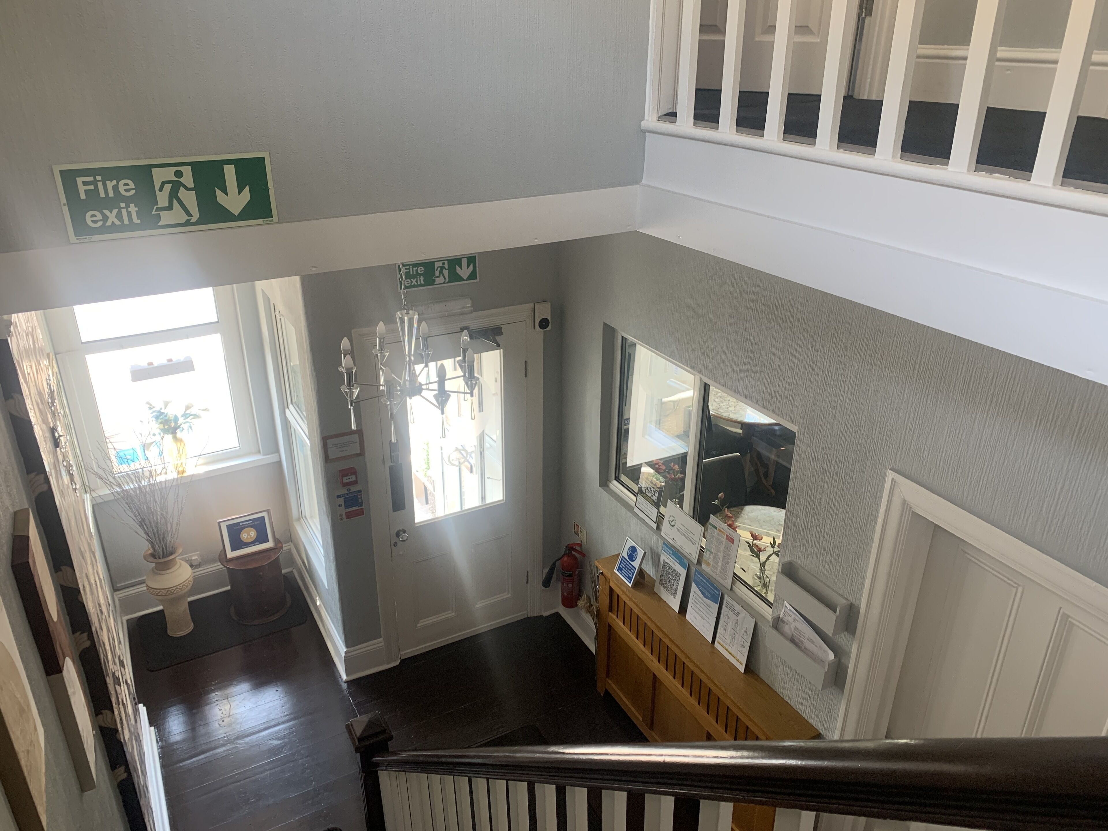 A staircase with a fire exit sign, a chandelier, and a reception desk with informational posters.