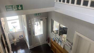 A staircase with a fire exit sign, a chandelier, and a reception desk with informational posters.