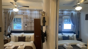 A hotel room with two beds, a wardrobe, a desk with a lamp, and a ceiling fan.