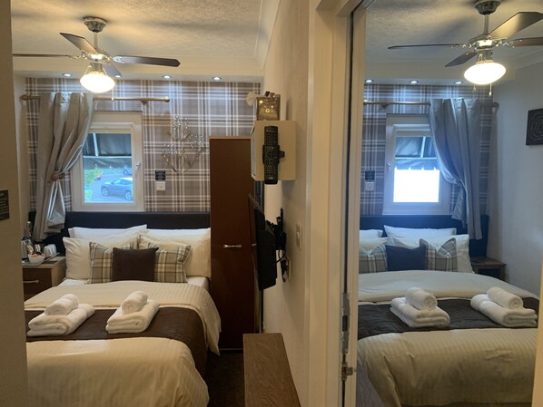 Habitación de hotel con dos camas, un armario, un escritorio con lámpara y un ventilador de techo.