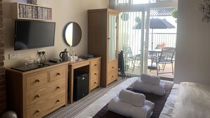 A hotel room with a bed, a desk with a TV, a wardrobe, and a view of the outdoor patio.