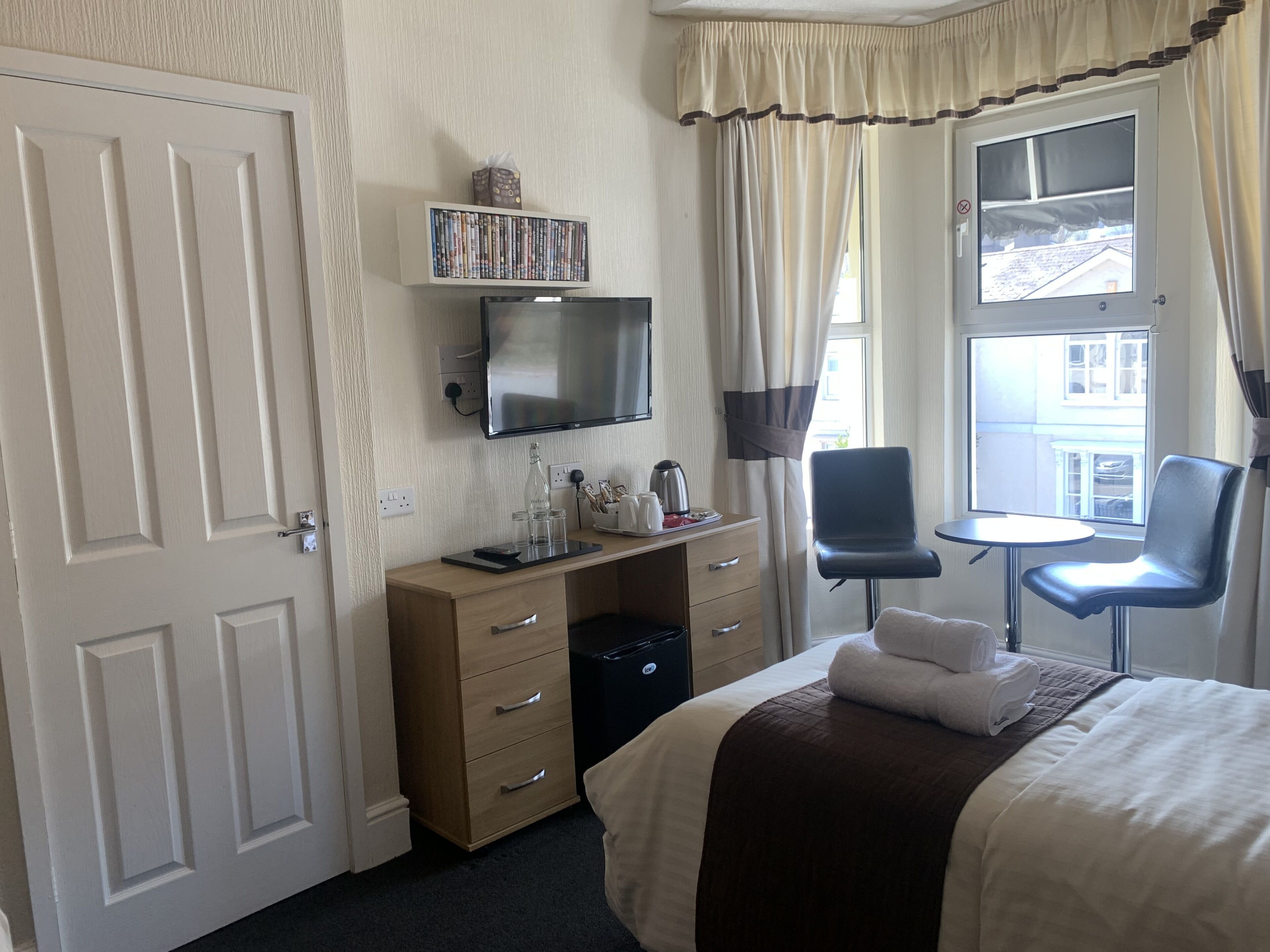 Une chambre d’hôtel avec un lit, un bureau avec une télévision, une chaise et une fenêtre avec des rideaux.