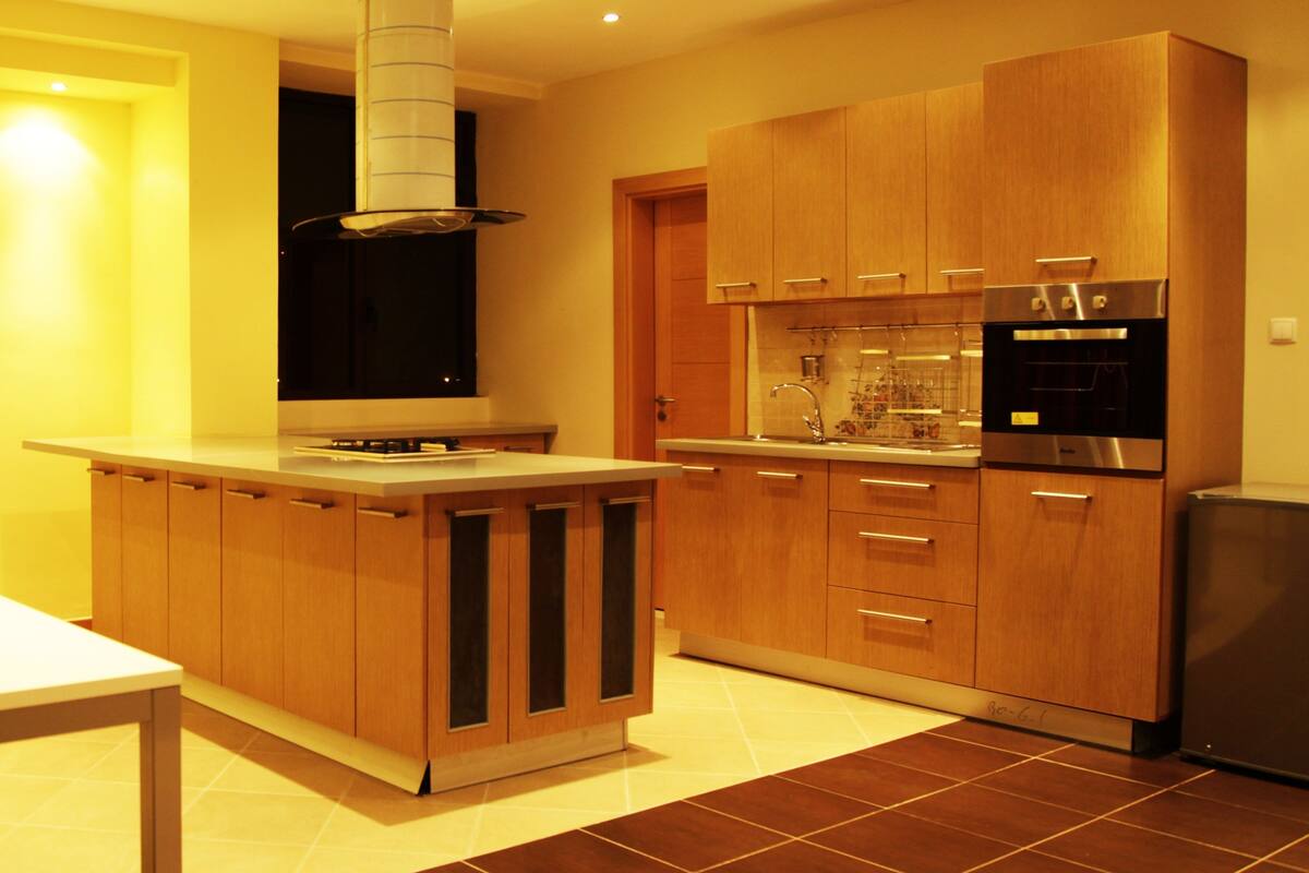 A modern kitchen with wooden cabinets, a built-in oven, and a large island with a range hood.