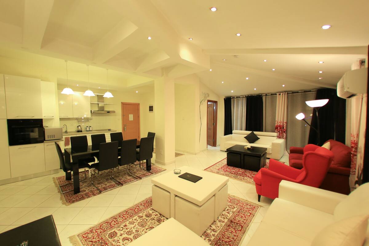 A modern living room with a dining area, a kitchen, and a seating area with red chairs.