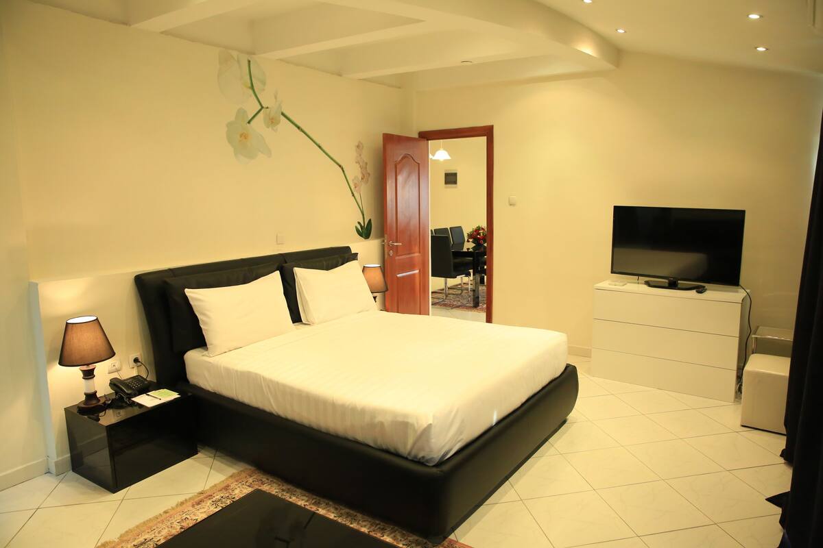 A bedroom with a bed, bedside table, lamp, and TV.