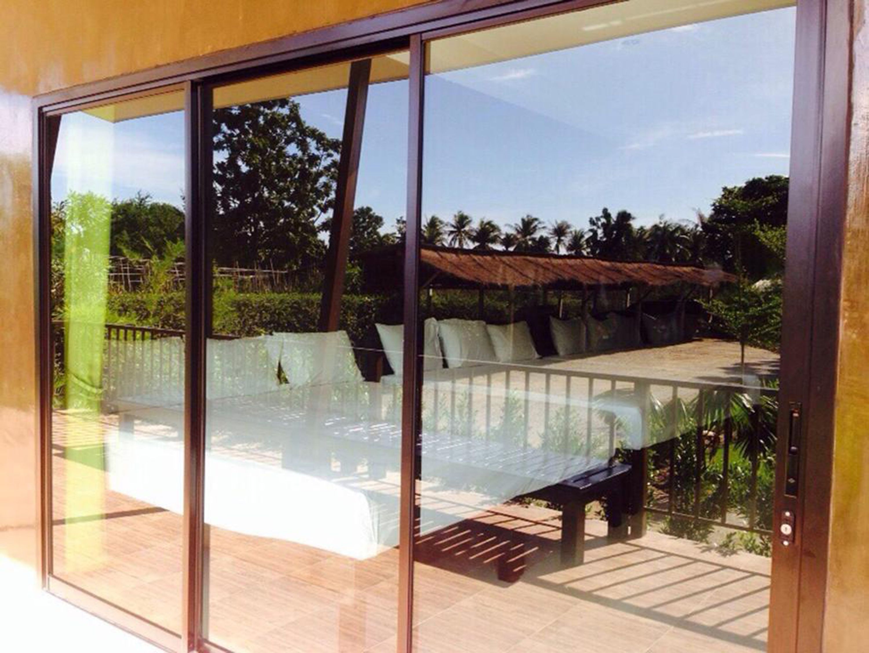 A modern outdoor seating area with a glass partition, wooden deck, and a view of a tropical landscape.