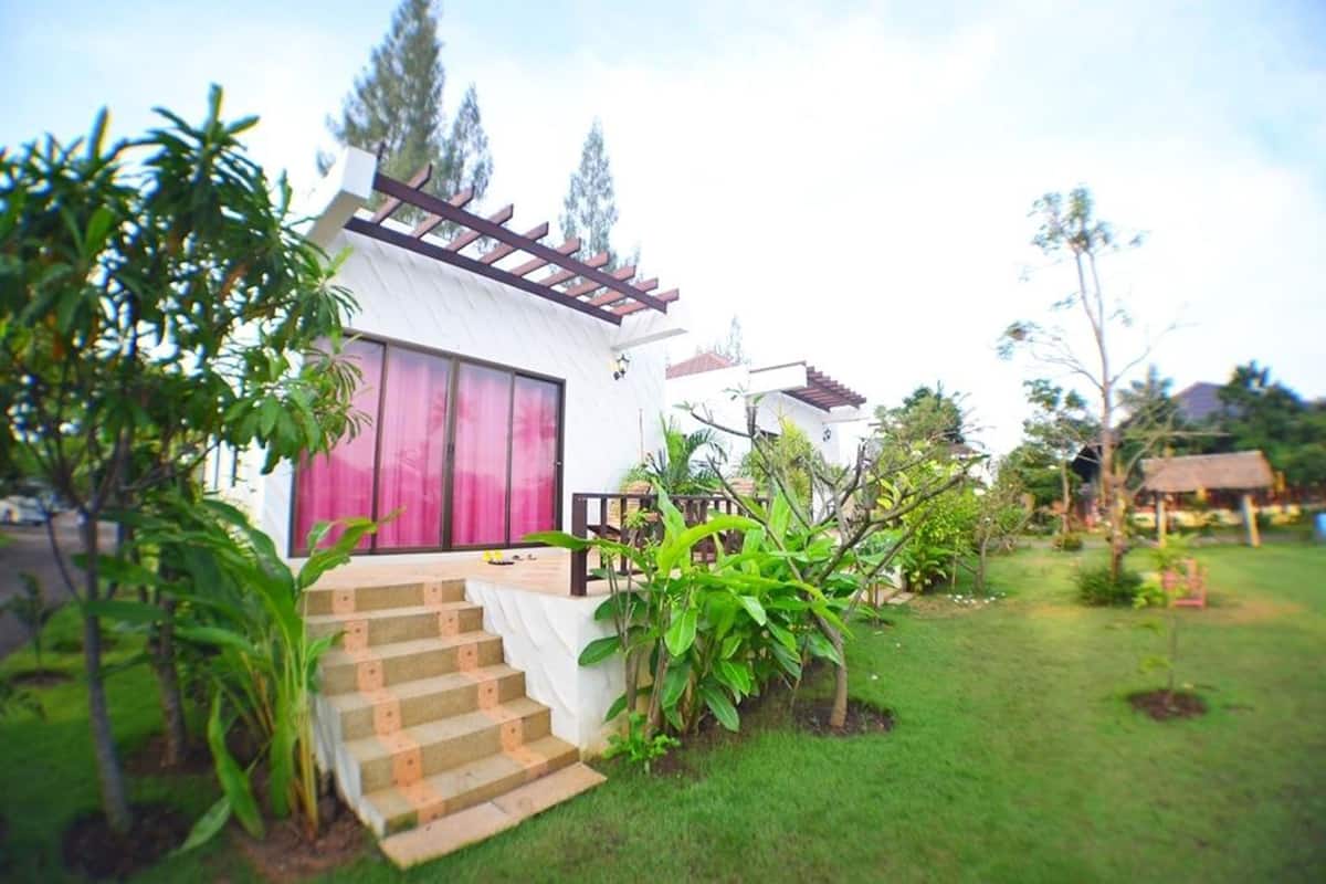 Uma casa com fachada branca, porta rosa e varanda pequena com degraus que levam à entrada.