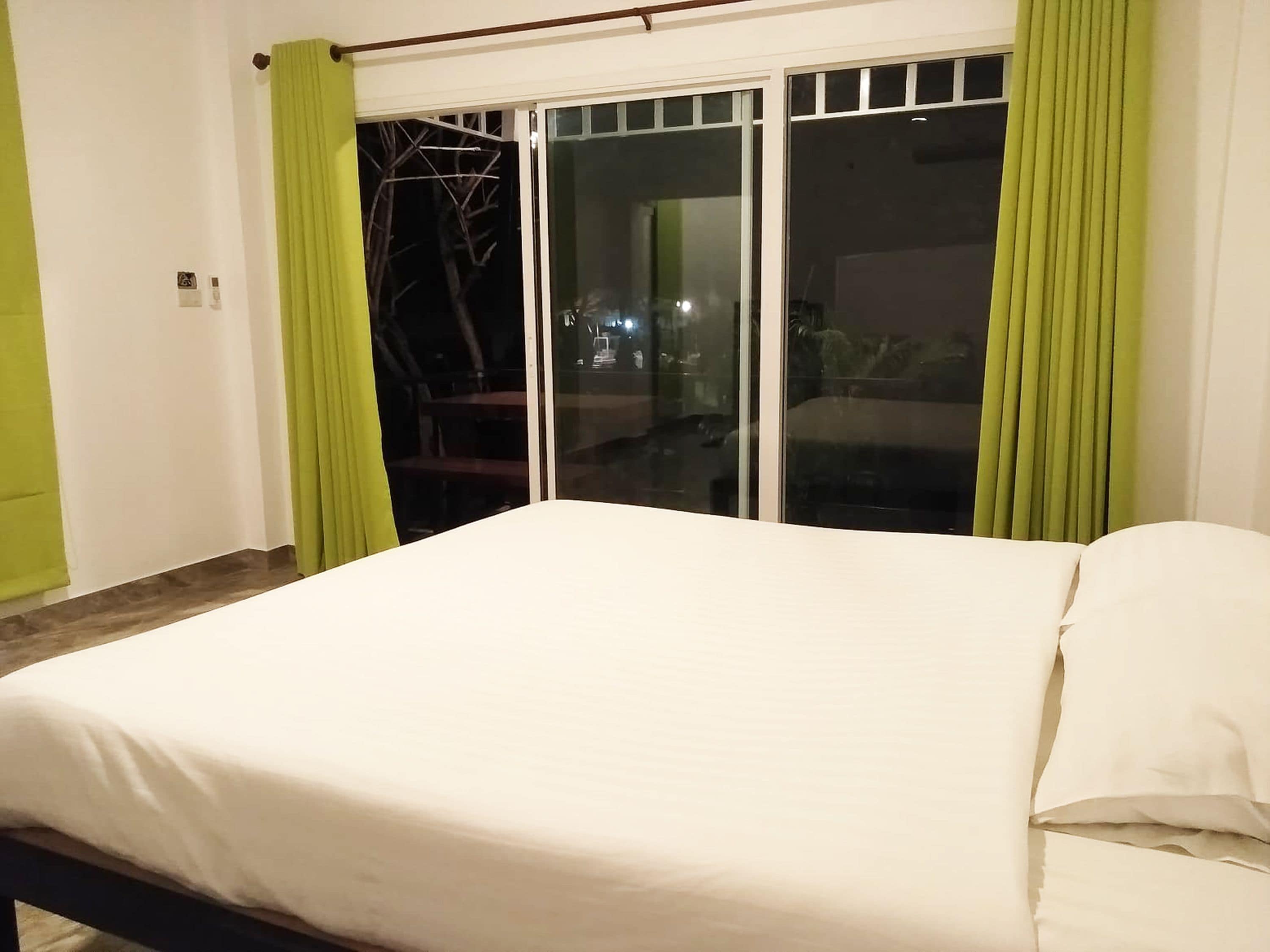 Une chambre à coucher avec un lit, des rideaux verts et une porte-fenêtre coulissante donnant sur un espace extérieur.