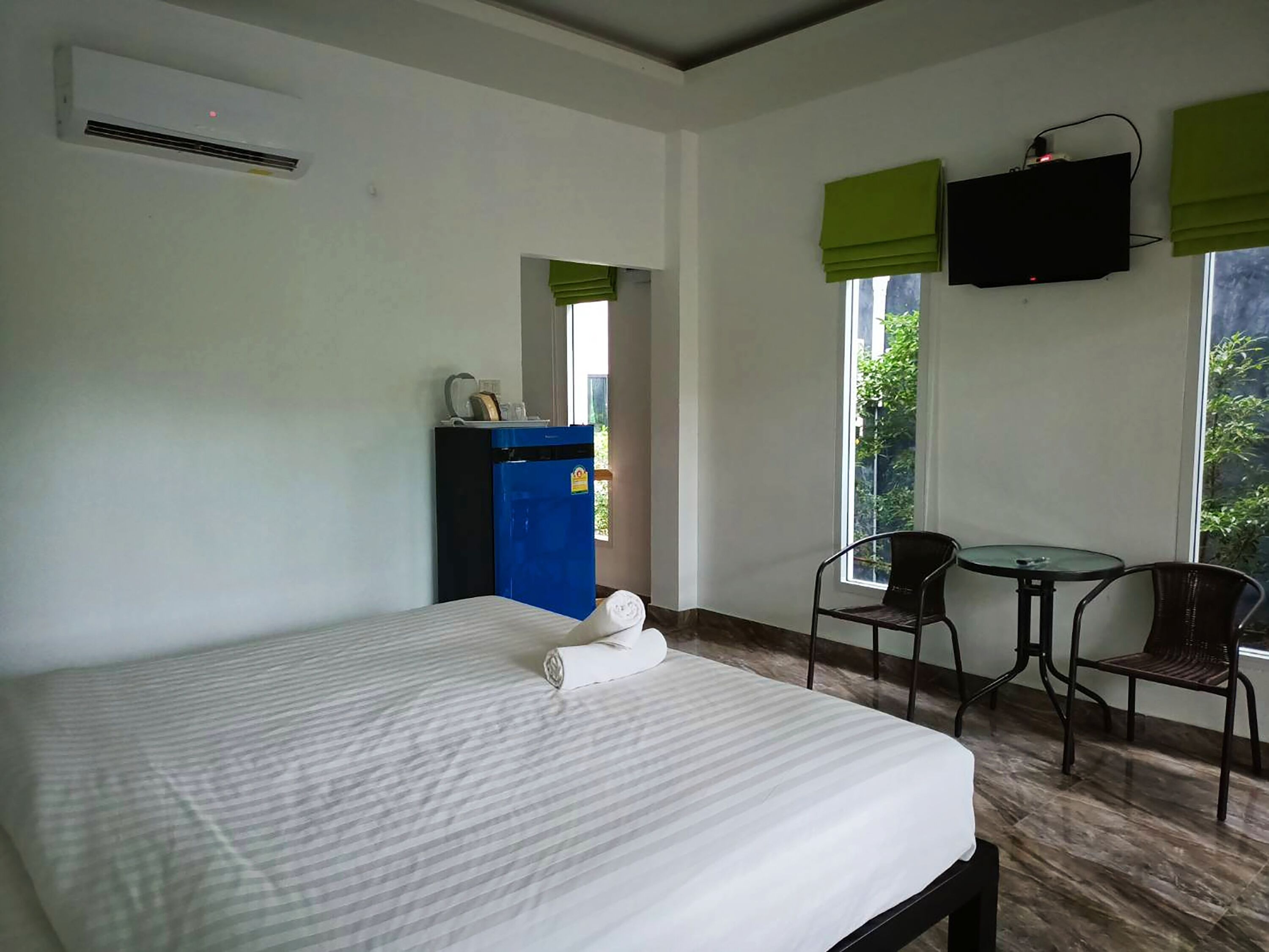 A hotel room with a bed, a desk, a chair, a TV, and a window with a view of greenery.