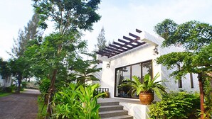Una casa moderna con fachada blanca, una pérgola de madera y una planta grande en maceta en la entrada.