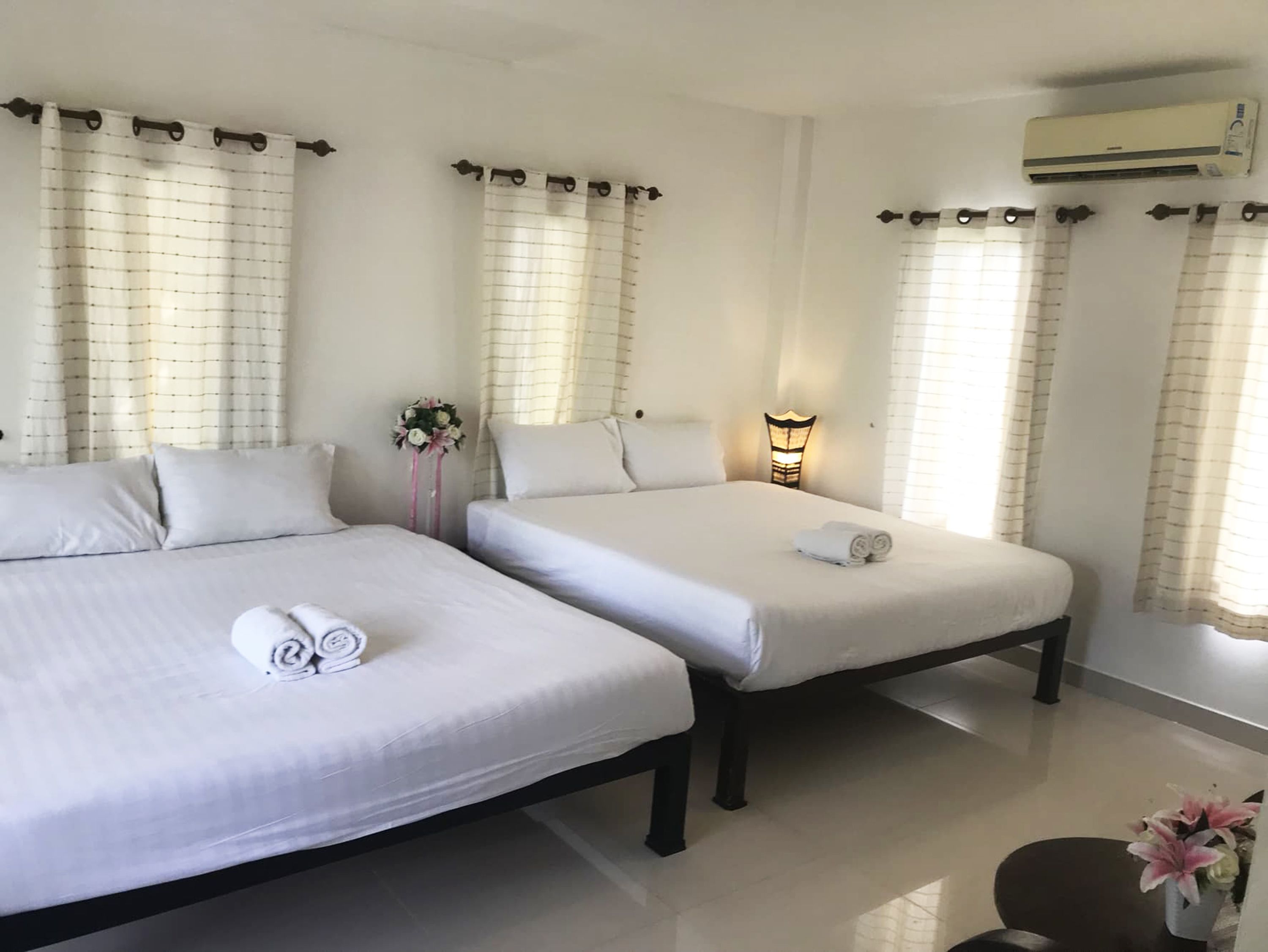 A hotel room with two beds, a nightstand with a lamp, and an air conditioning unit.