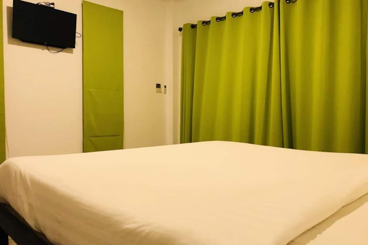 Quarto com cama, televisão na parede e cortinas verdes.