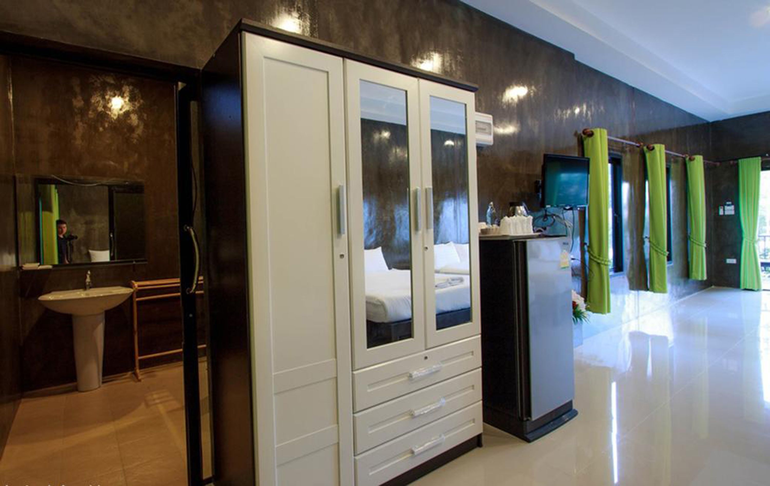 A hotel room with a large wardrobe, a sink, a bed, and a television.