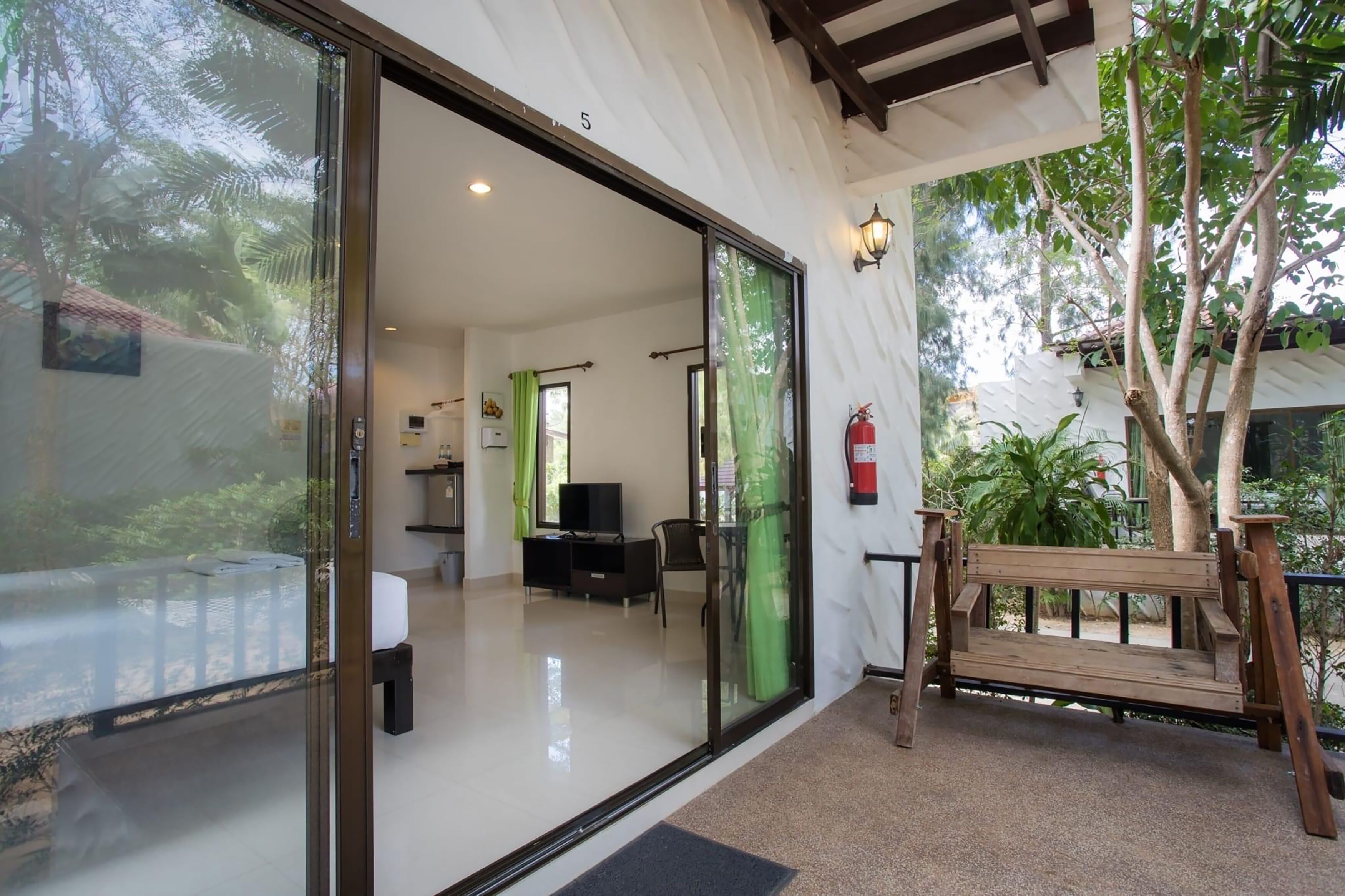A modern hotel room with a sliding glass door leading to a balcony, a small kitchenette, and a seating area with a bench and table.