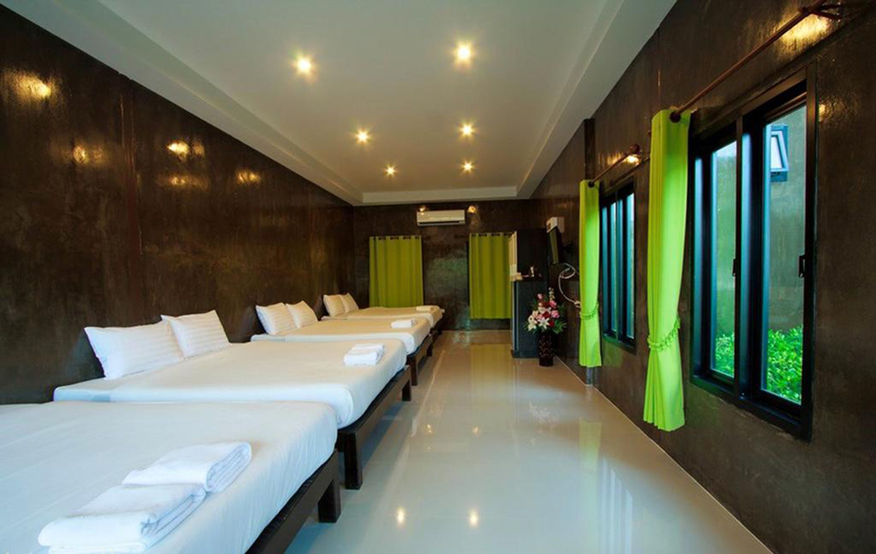 Quarto de hotel com três camas, banheiro e janelas amplas com cortinas.