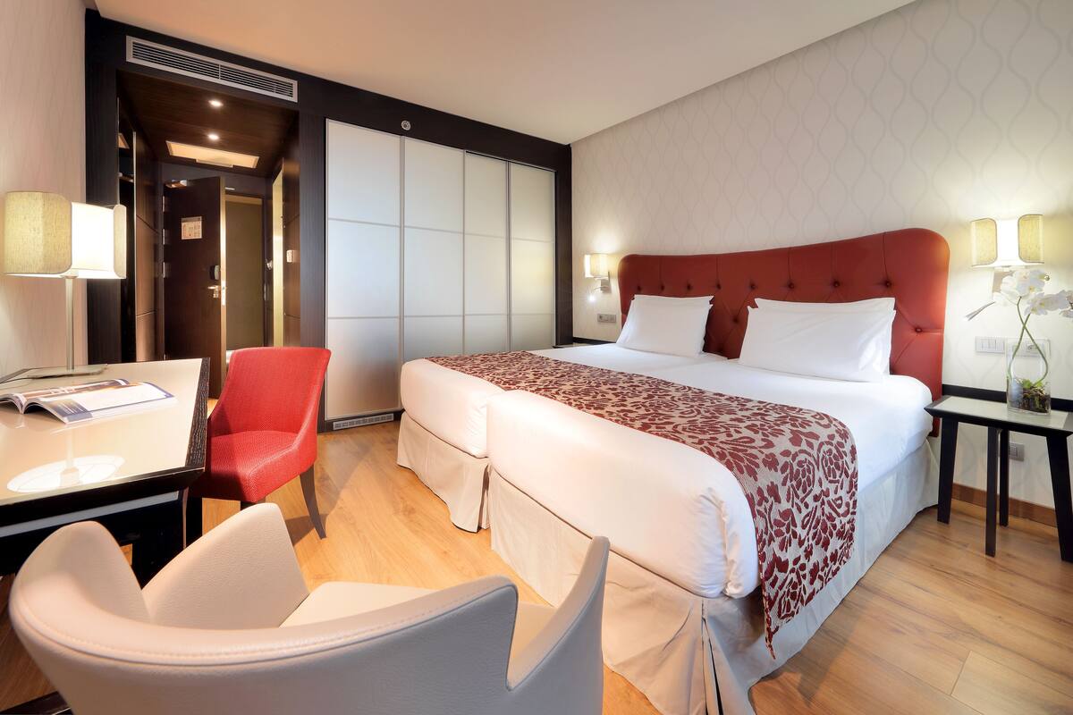 Una habitación de hotel con cama, escritorio, silla y una mesita de noche con lámpara.