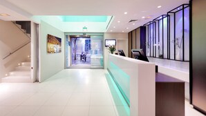 Un hall d’hôtel moderne avec un comptoir d’accueil, un escalier et une porte vitrée donnant sur la rue.