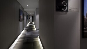 Un couloir d’hôtel moderne avec un sol à motifs à carreaux, un panneau indiquant le numéro « 3 » et un tableau encadré accroché au mur.