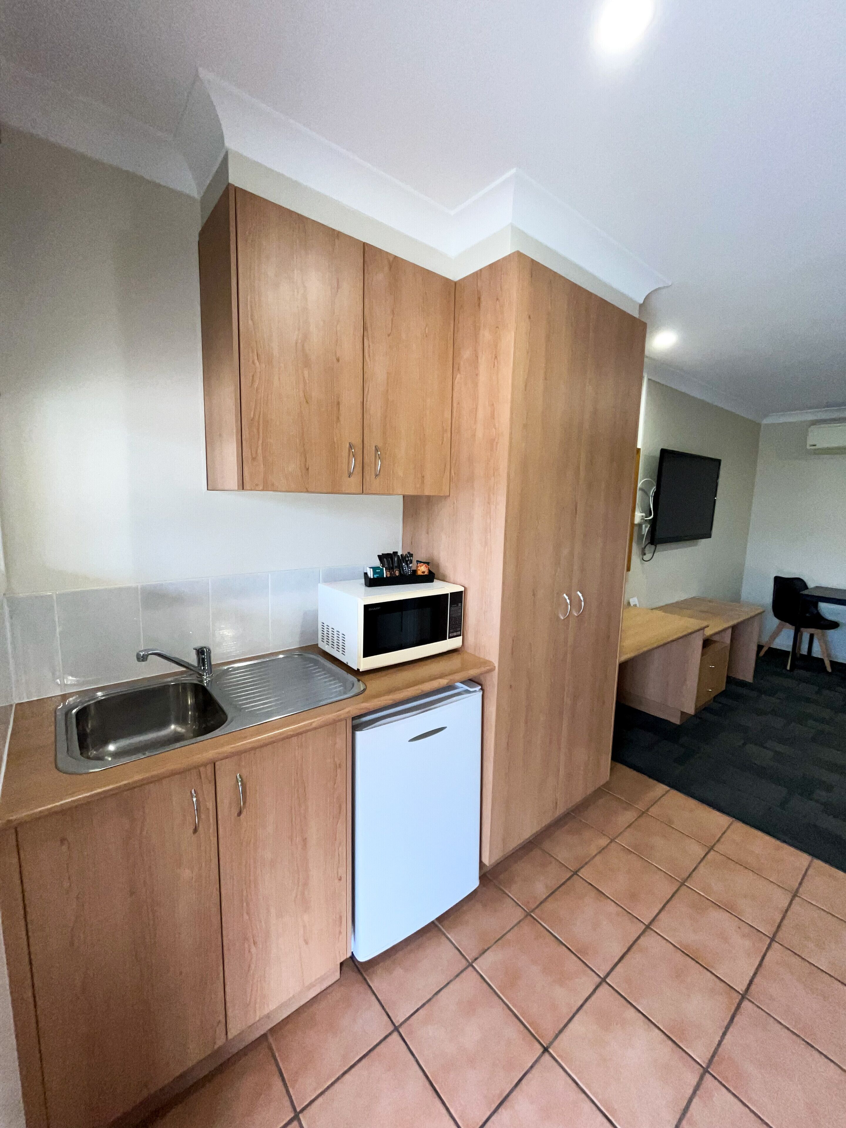 A compact kitchen with wooden cabinets, a built-in sink, a microwave, and a small refrigerator.