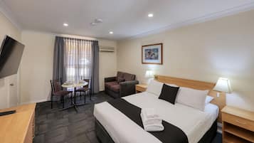 Ein Hotelzimmer mit einem Bett, Nachttischen, einem Schreibtisch, einem Sessel sowie einem kleinen Tisch mit Stuhl und einem Fernseher.