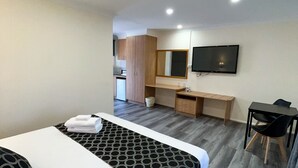 Hotellihuone, jossa on sänky, työpöytä, tuoli, televisio ja pieni keittonurkkaus.