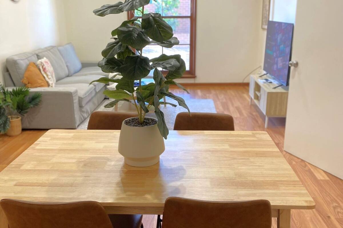 A dining area with a wooden table, two chairs, and a potted plant.