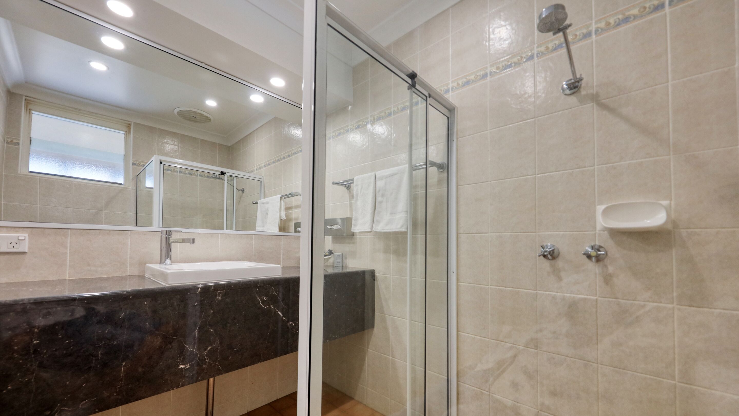 A modern bathroom with a glass-enclosed shower, a marble sink, and a large mirror.