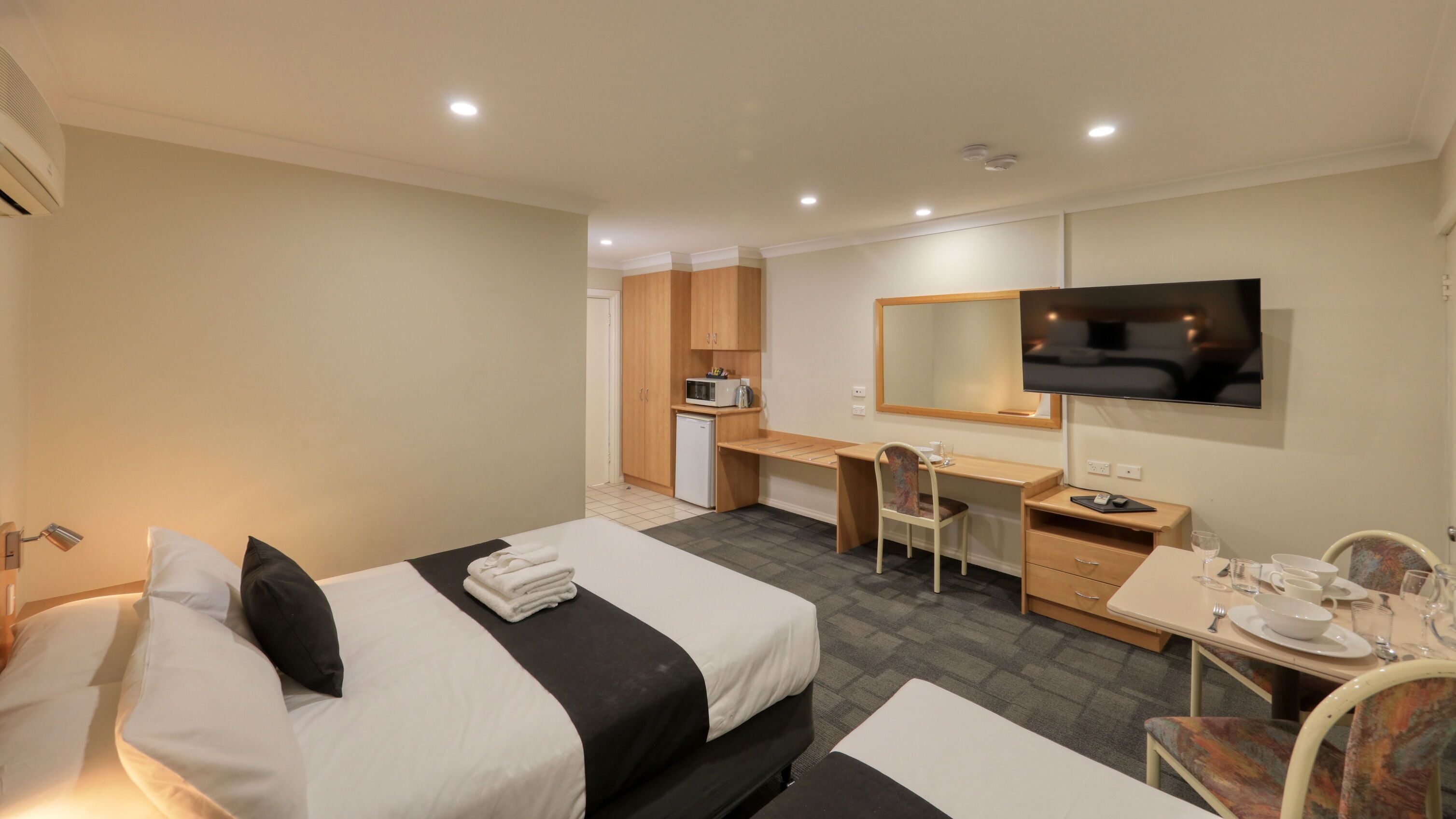 Habitación de hotel con dos camas, un escritorio, una silla, un televisor y una pequeña kitchenette.