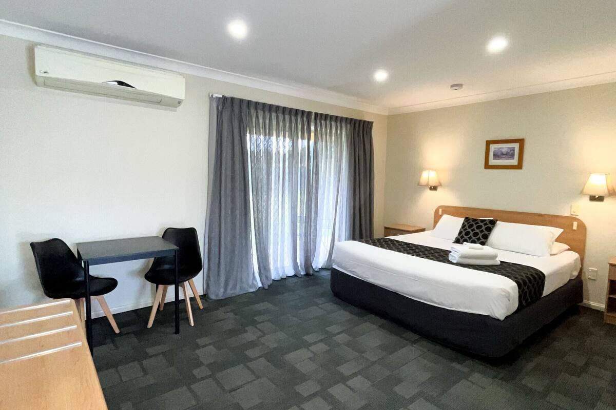 A hotel room with a bed, desk, chairs, and a window with curtains.