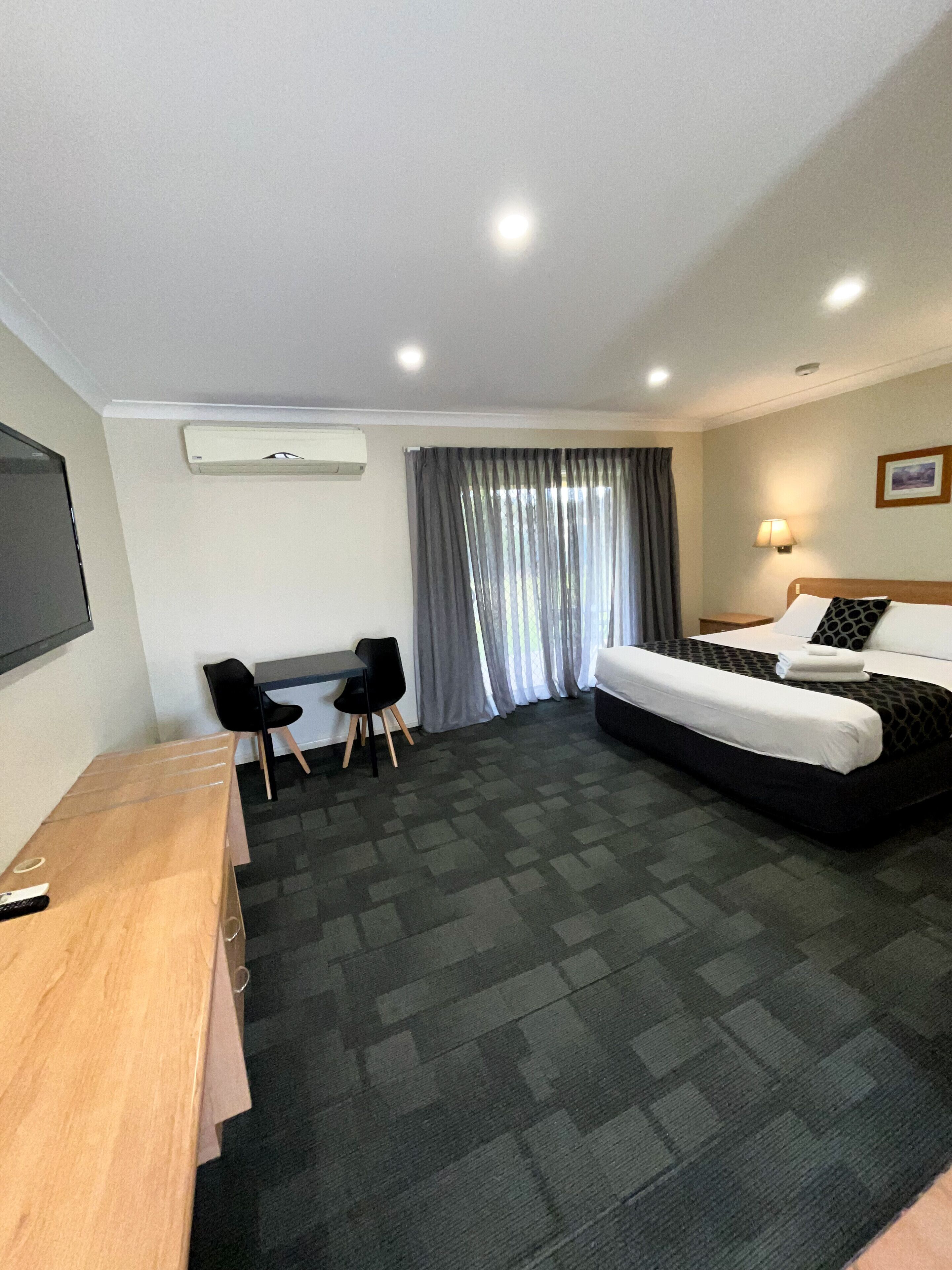 A hotel room with a bed, a desk, two chairs, a TV, and a window with curtains.
