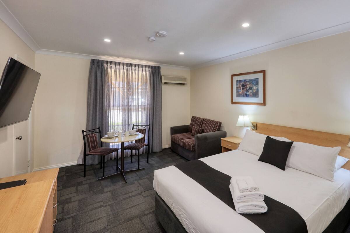 A hotel room with a bed, a desk, a chair, a table, and a TV.