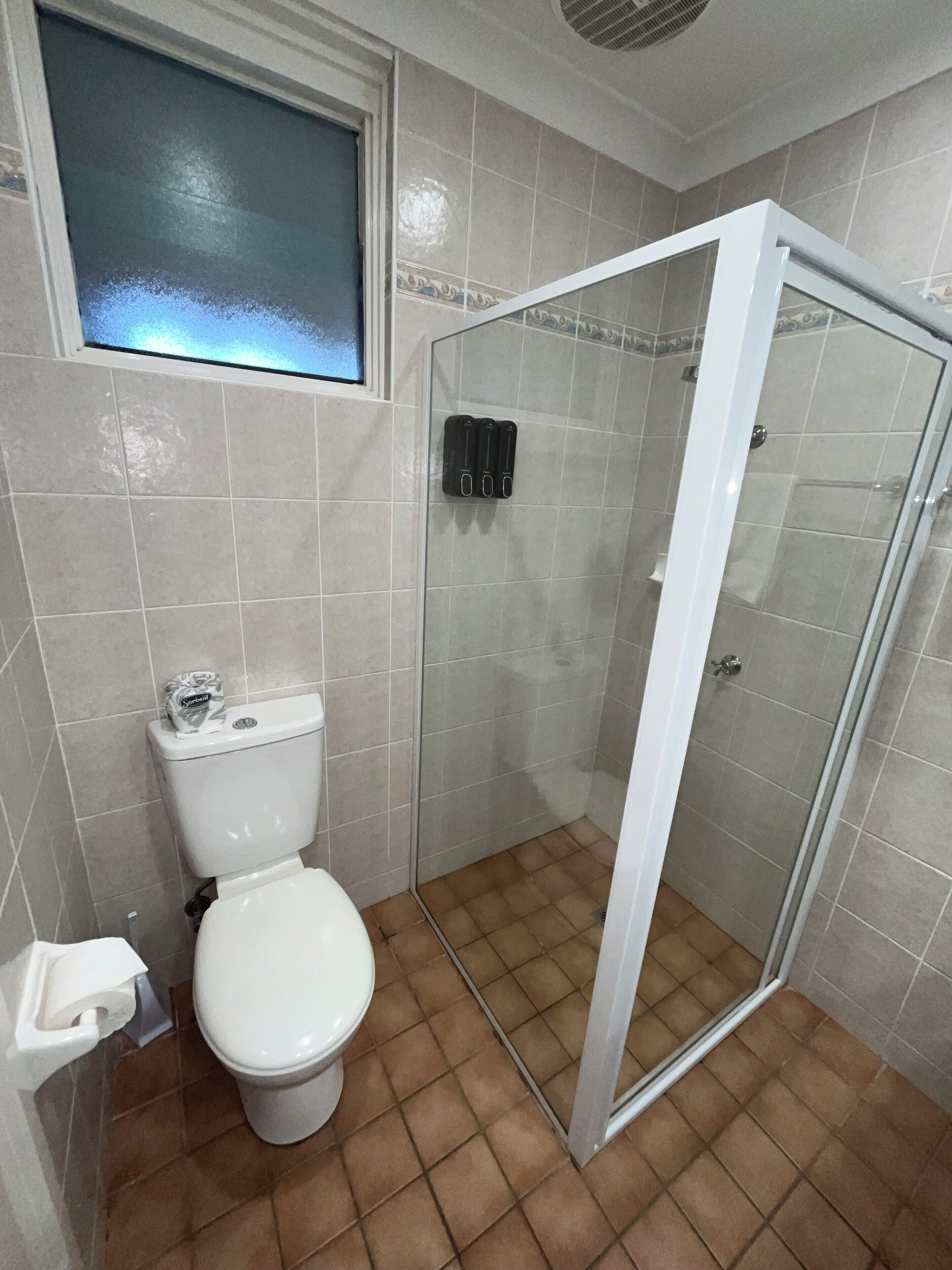 A bathroom with a toilet, a shower with a glass door, and a window above the toilet.