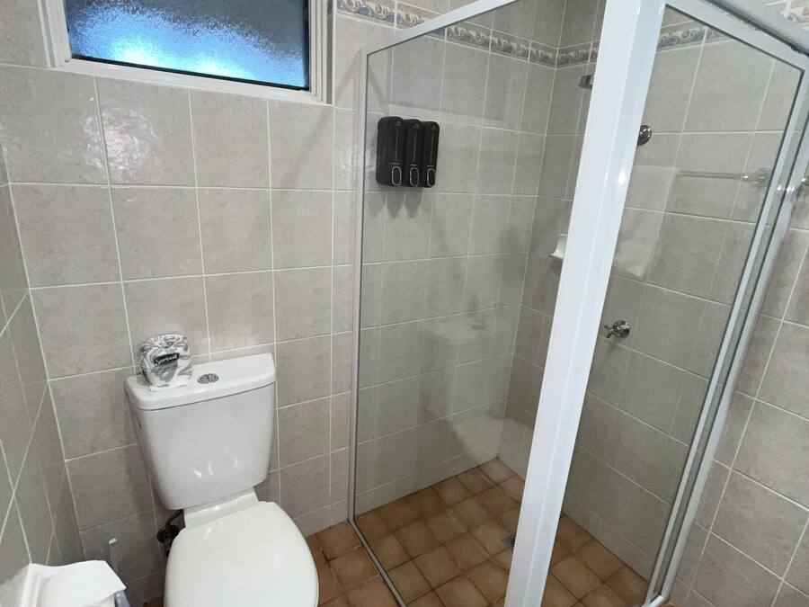 A bathroom with a toilet, a shower with a glass door, and a window above the toilet.