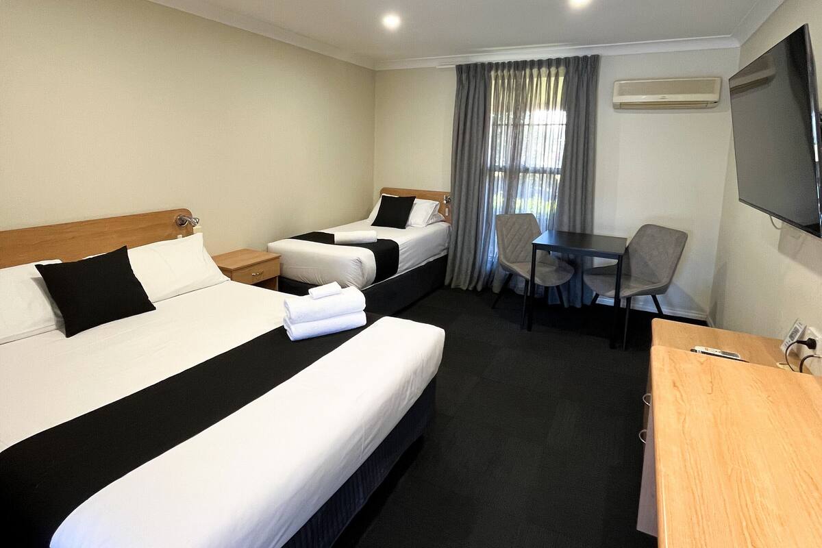 A hotel room with two beds, a desk, a chair, and a TV.