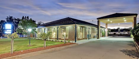 A modern building with a covered entrance and a well-lit lawn area.