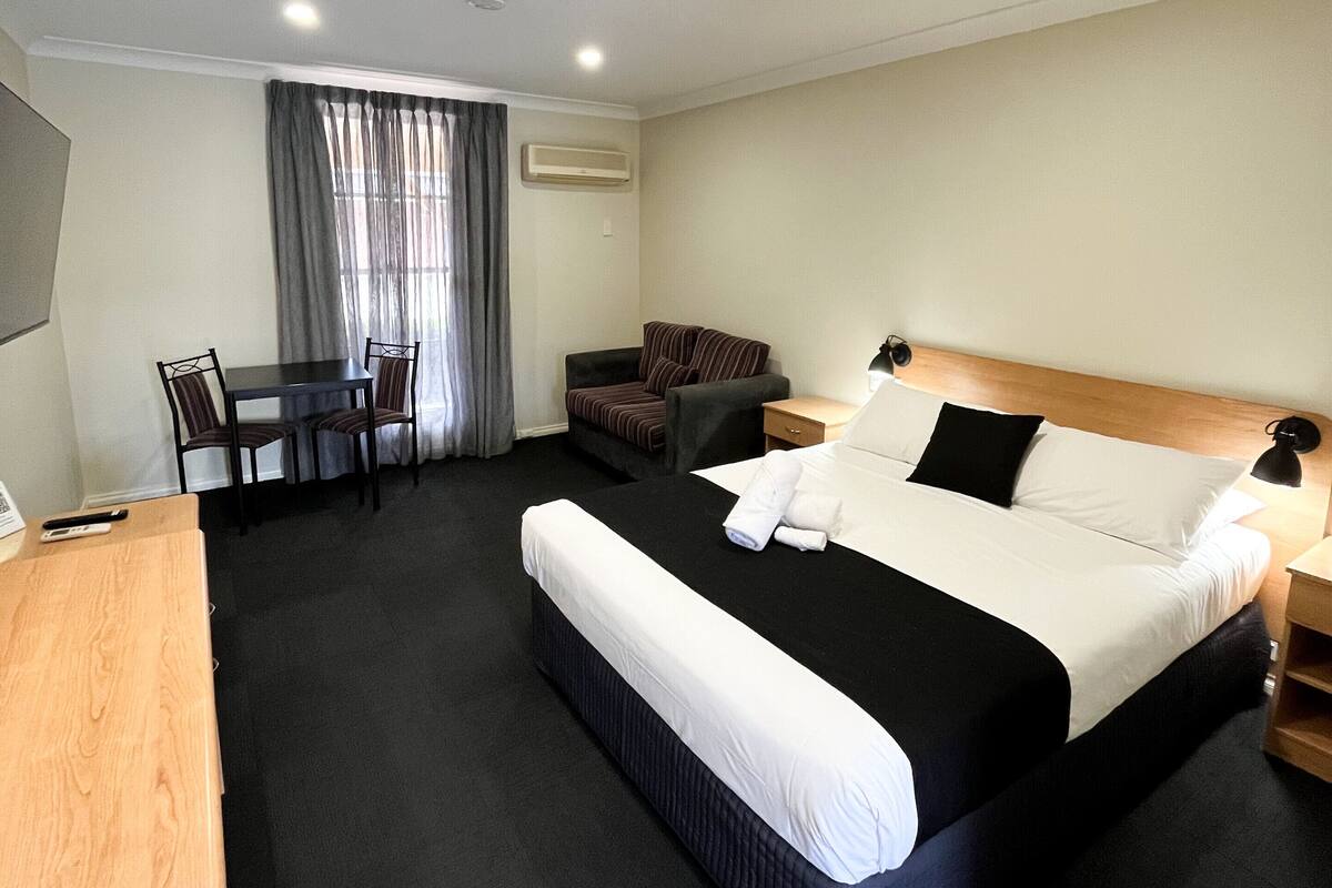 A hotel room with a large bed, a desk, a chair, and a small table.